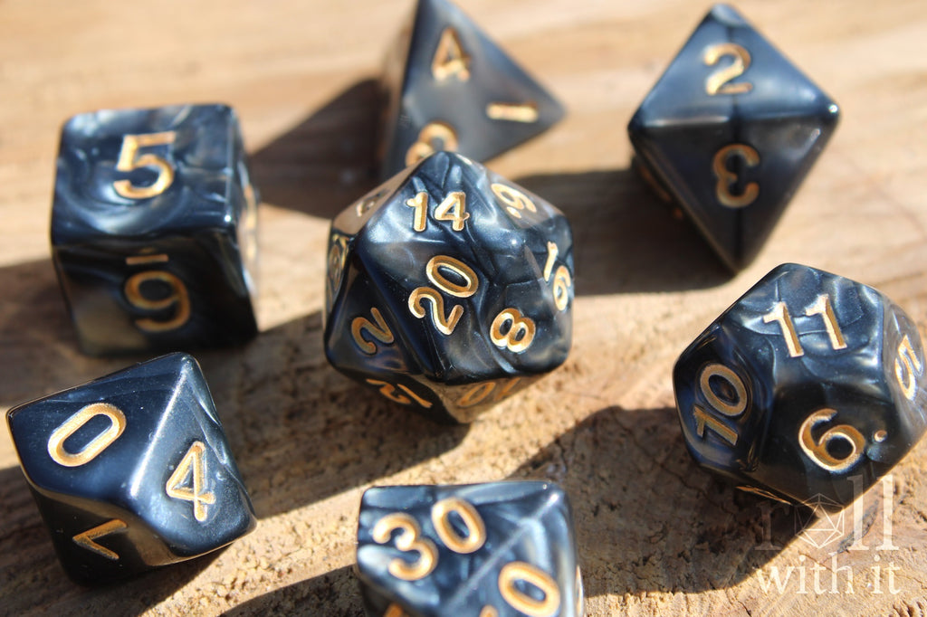 Set of black swirling polyhedral DnD dice with gold numbers on a wooden surface