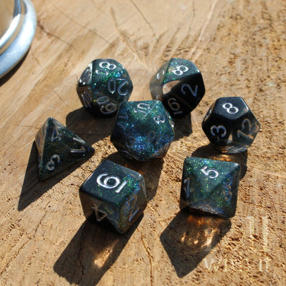 Set of black blue green star polyhedral dice with glittery finish on a wooden surface