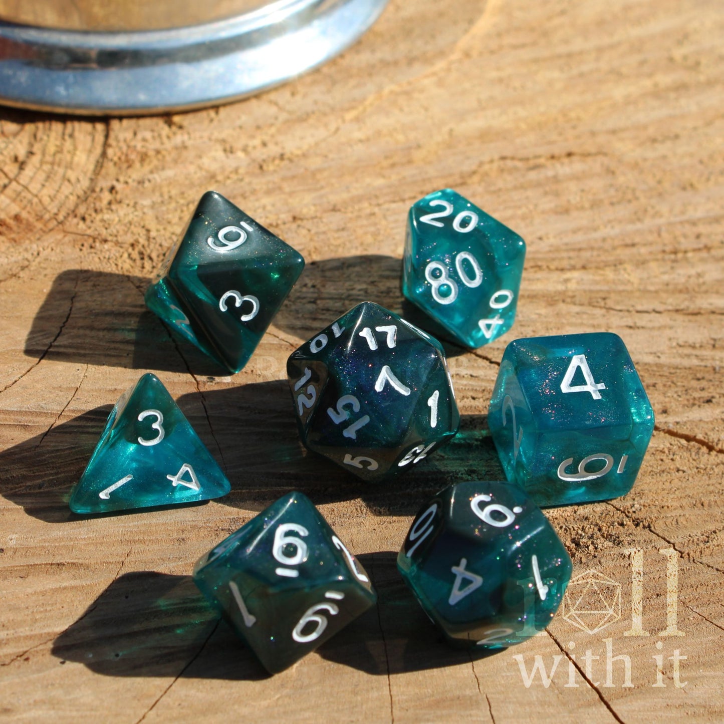 Set of dark teal glittery dice on a wooden surface with white numbers