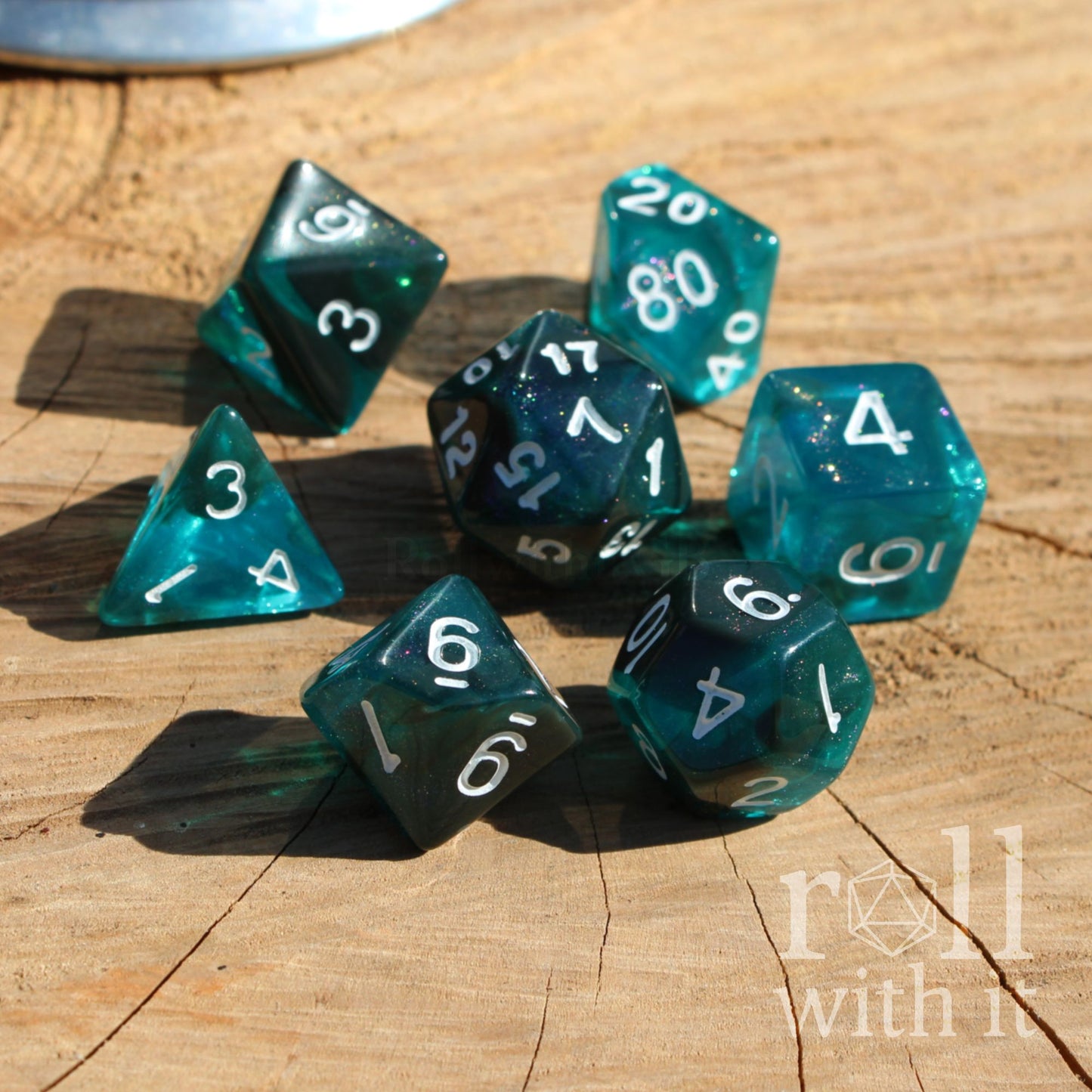 Set of teal polyhedral dice with white numbers on a wooden surface, featuring 'roll with it' branding.