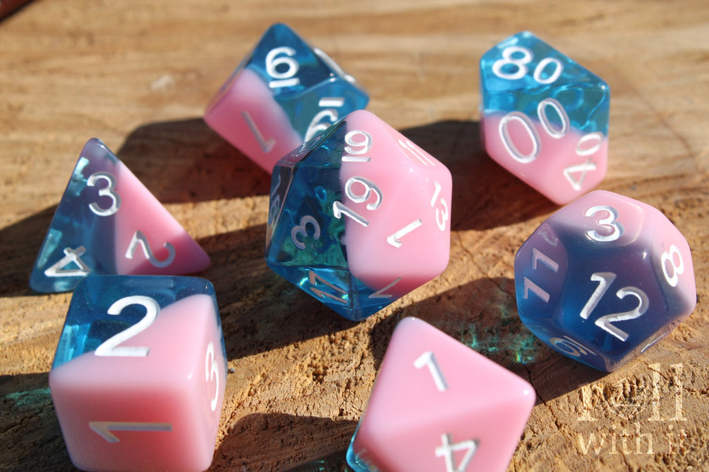 Set of bubblegum pink and clear blue polyhedral roleplaying dice on a wooden surface