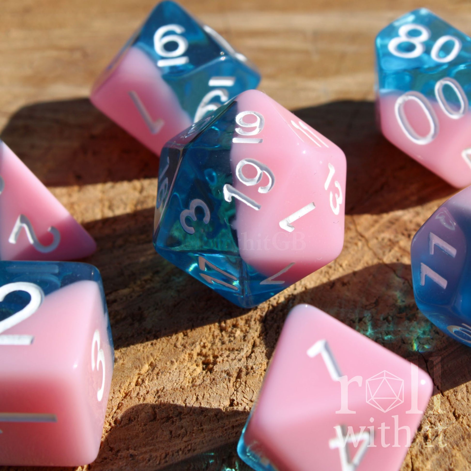Set of bubblegum pink and clear blue polyhedral roleplaying dice on a wooden surface