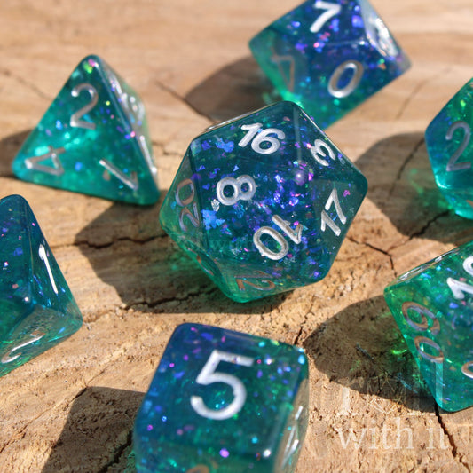 Set of glittery and shining blue and green polyhedral DND dice with silver leaf inside on a wooden surface