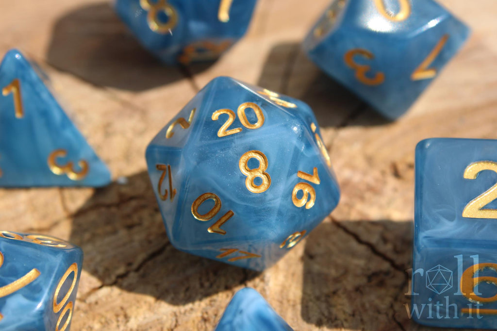 Set of jade blue translucent polyhedral roleplaying dice with gold numbers on a wooden surface