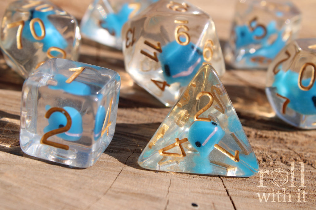 Set of clear polyhedral DnD dice with a small blue whale inside on a wooden surface