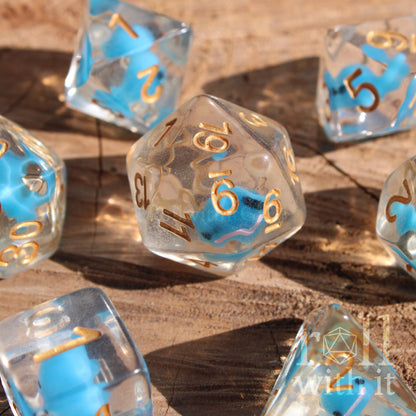Set of clear polyhedral DnD dice with a small blue whale inside on a wooden surface