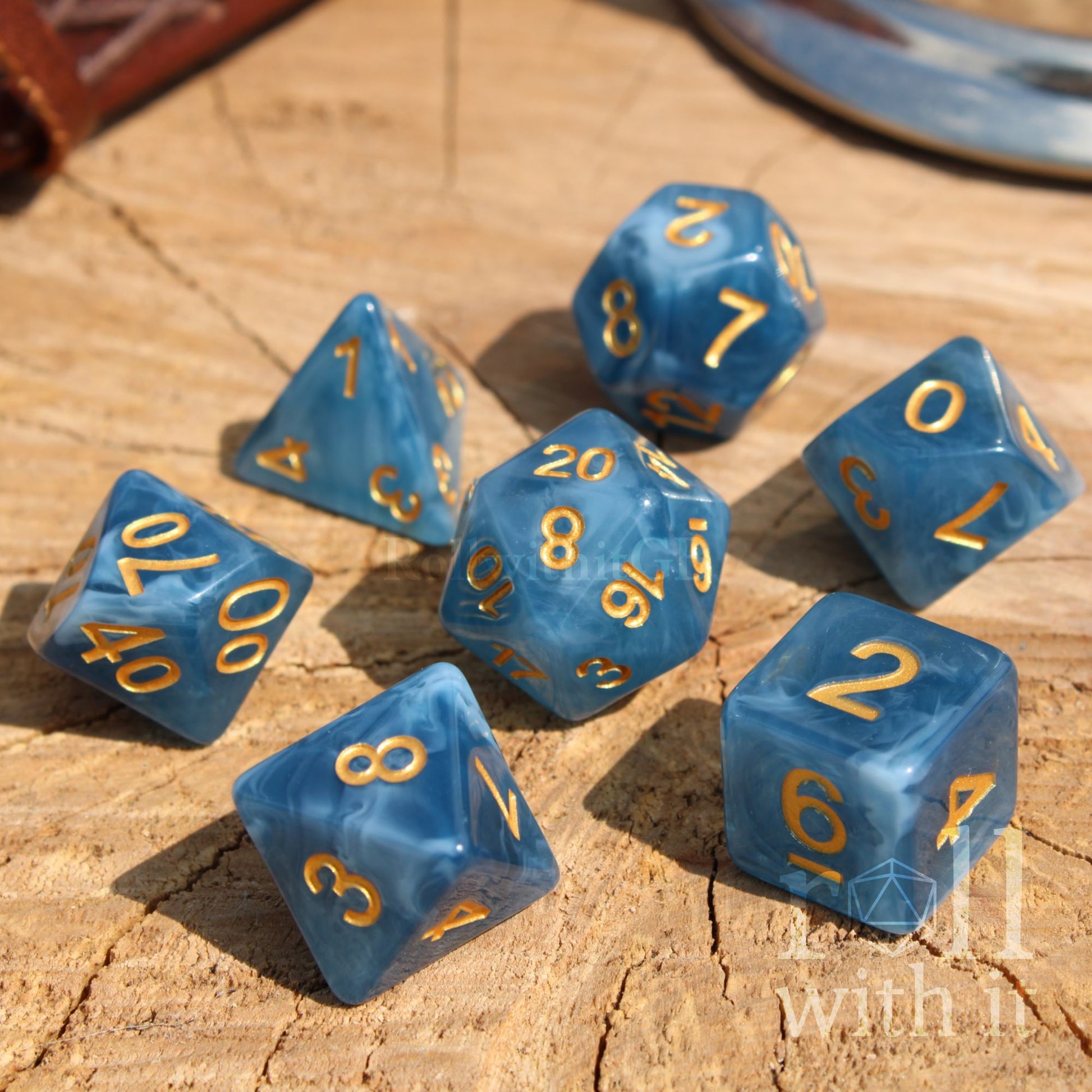 Blue swirling translucent polyhedral dice set with gold numbers on a wooden surface