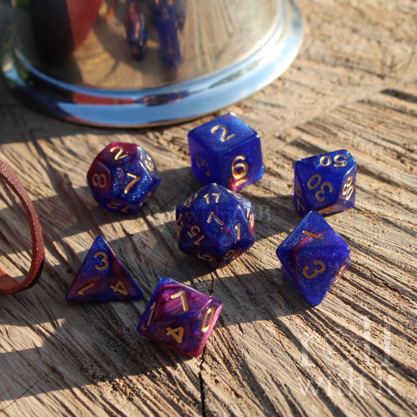 Set of blue and purple glitter polyhedral dice on a wooden surface with a metallic cup in the background.