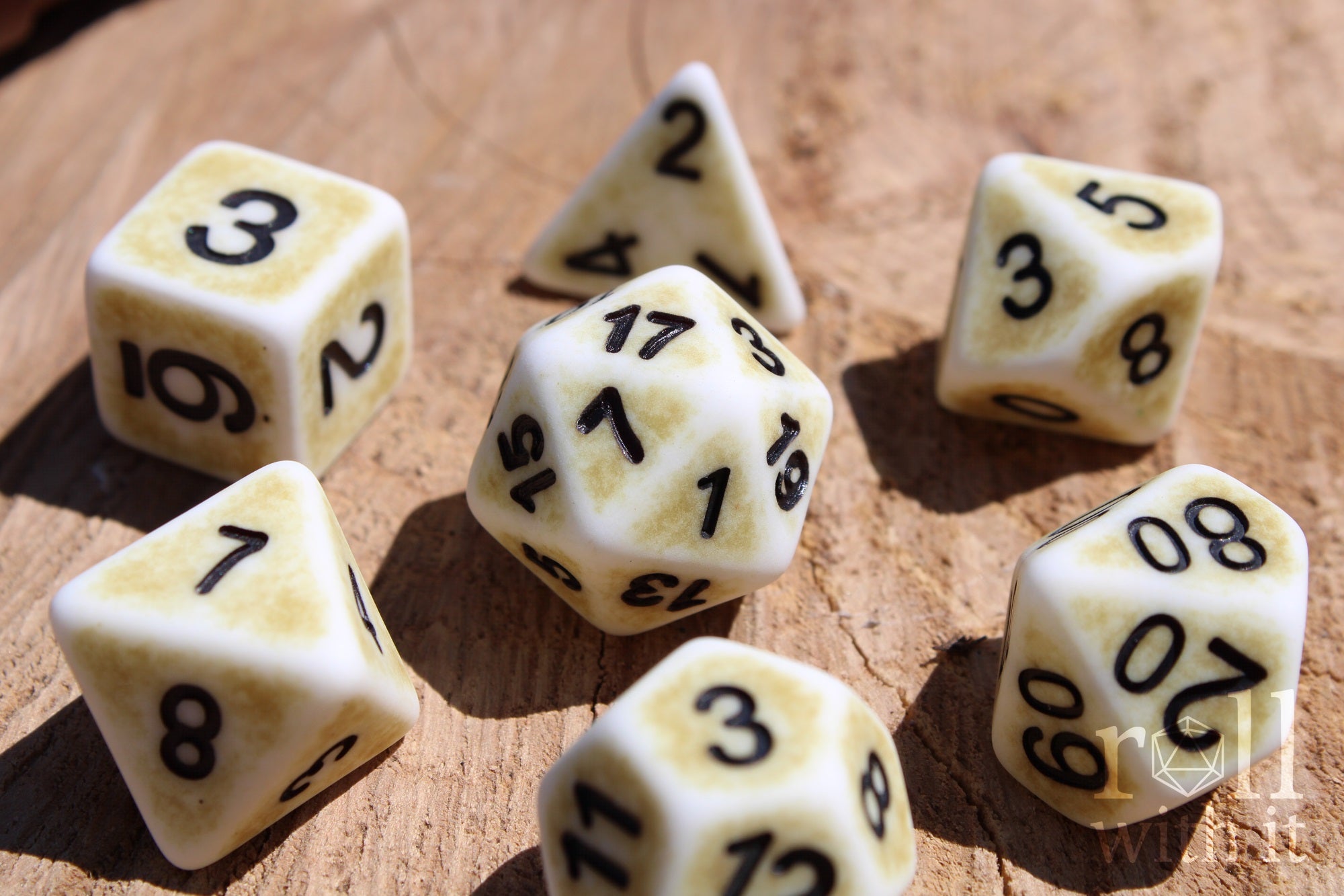 Set of creamy bone white matte roleplaying dice with a worn looking surface, with black numbers on a wooden surface