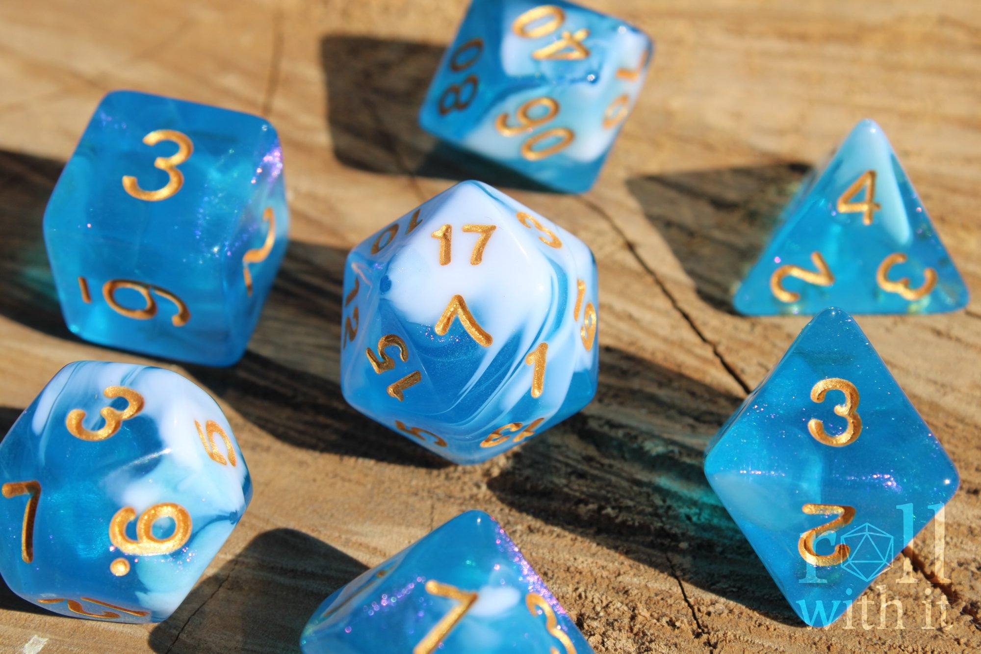 Set of blue and white glittery polyhedral dice with gold numbers on a wooden surface