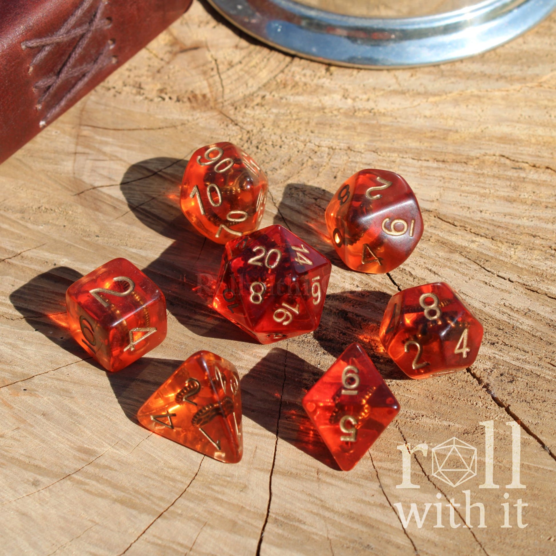 Set of 7 red orange transparent dice with golden cogs inside on a wooden surface with 'roll with it' text.