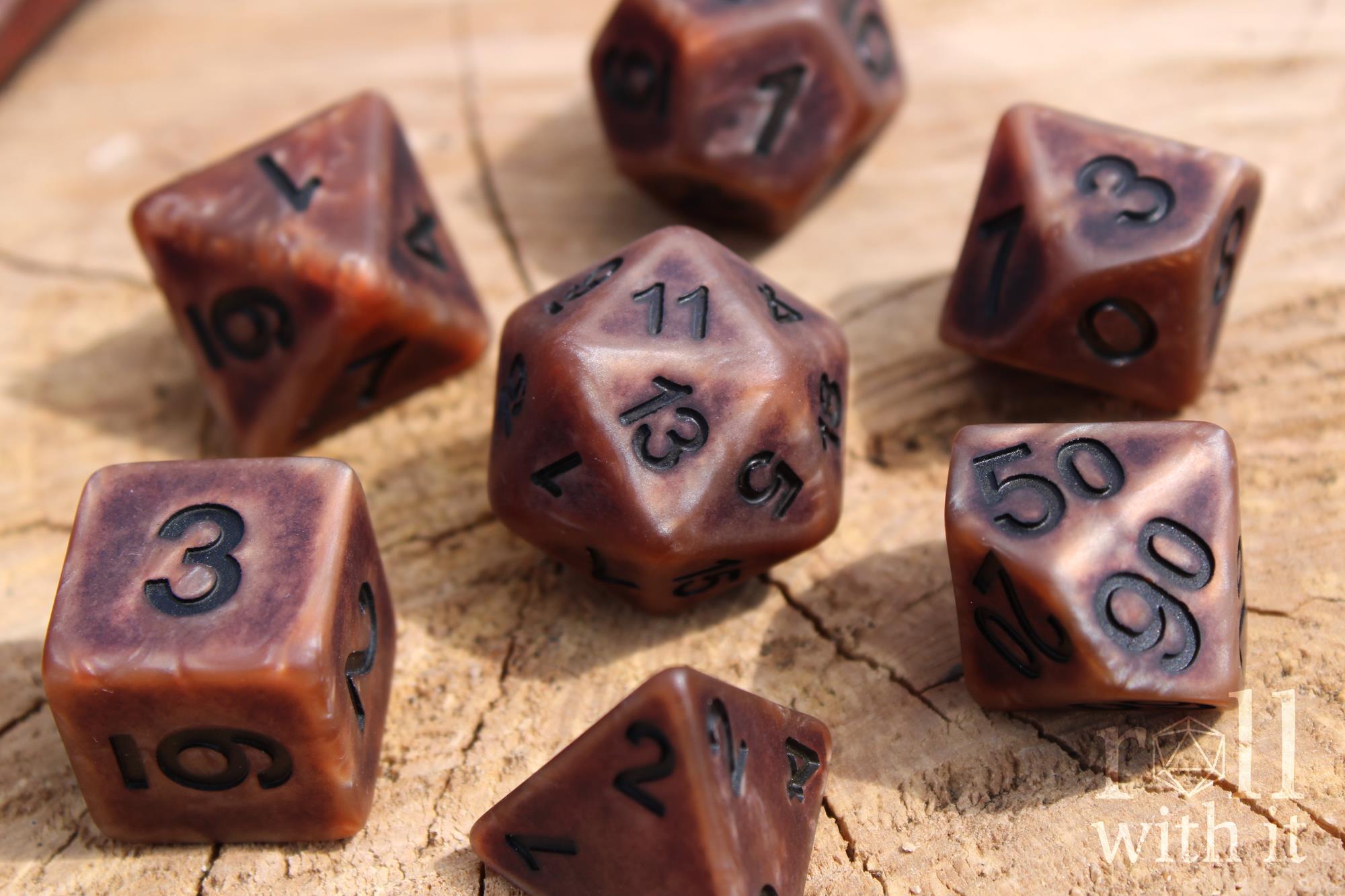 Set of matte bronze copper polyhedral roleplaying dice with a worn look and black numbers on a wooden surface