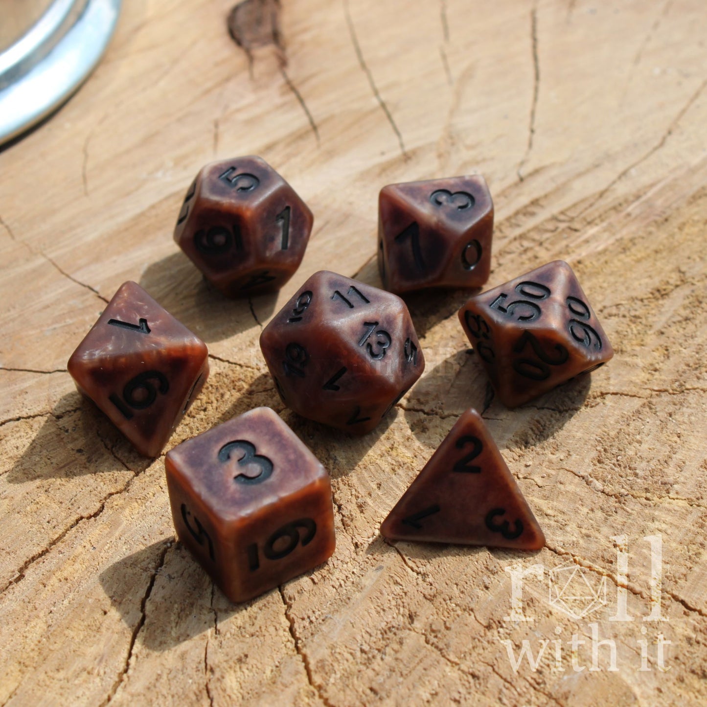 Set of bronze polyhedral dice on a wooden surface with 'roll with it' text.