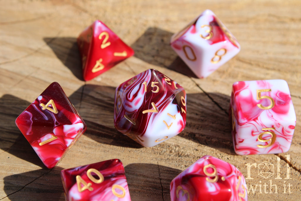 A set of 7 creamy cherry red and white swirling polyhedral tabletop roleplaying dice on an oak base.
