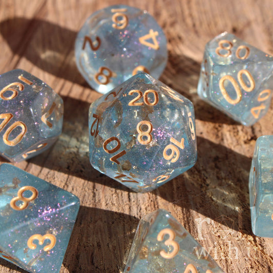 Set of clear blue and gold foil dice with gold numbers on a wooden surface
