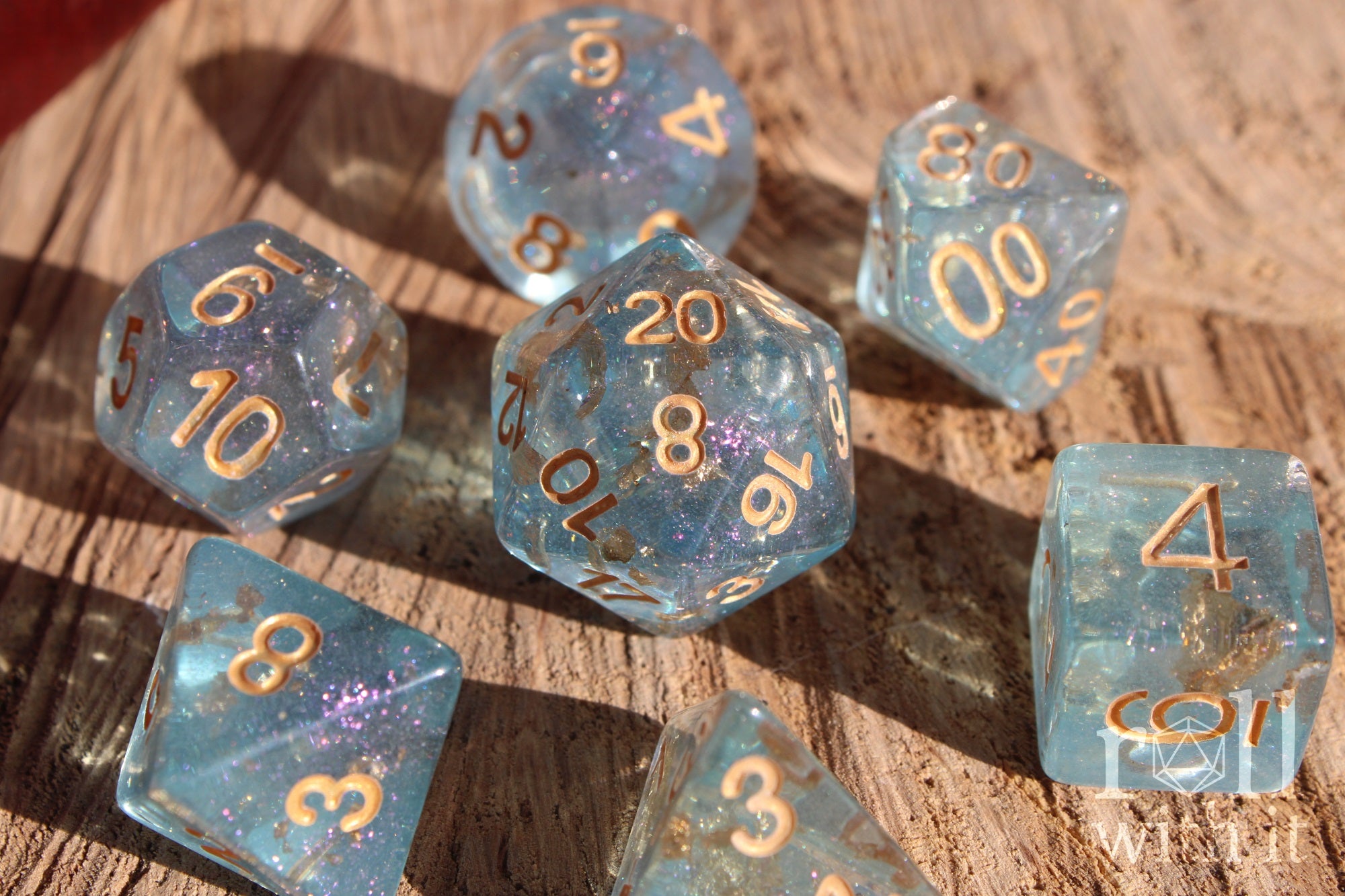 Set of clear blue and gold foil dice with gold numbers on a wooden surface