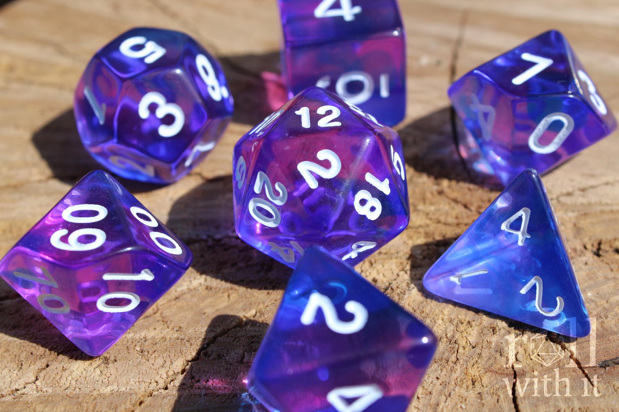 Set of clear blue and indigo purple polyhedral roleplaying dice with white numbers on a wooden surface