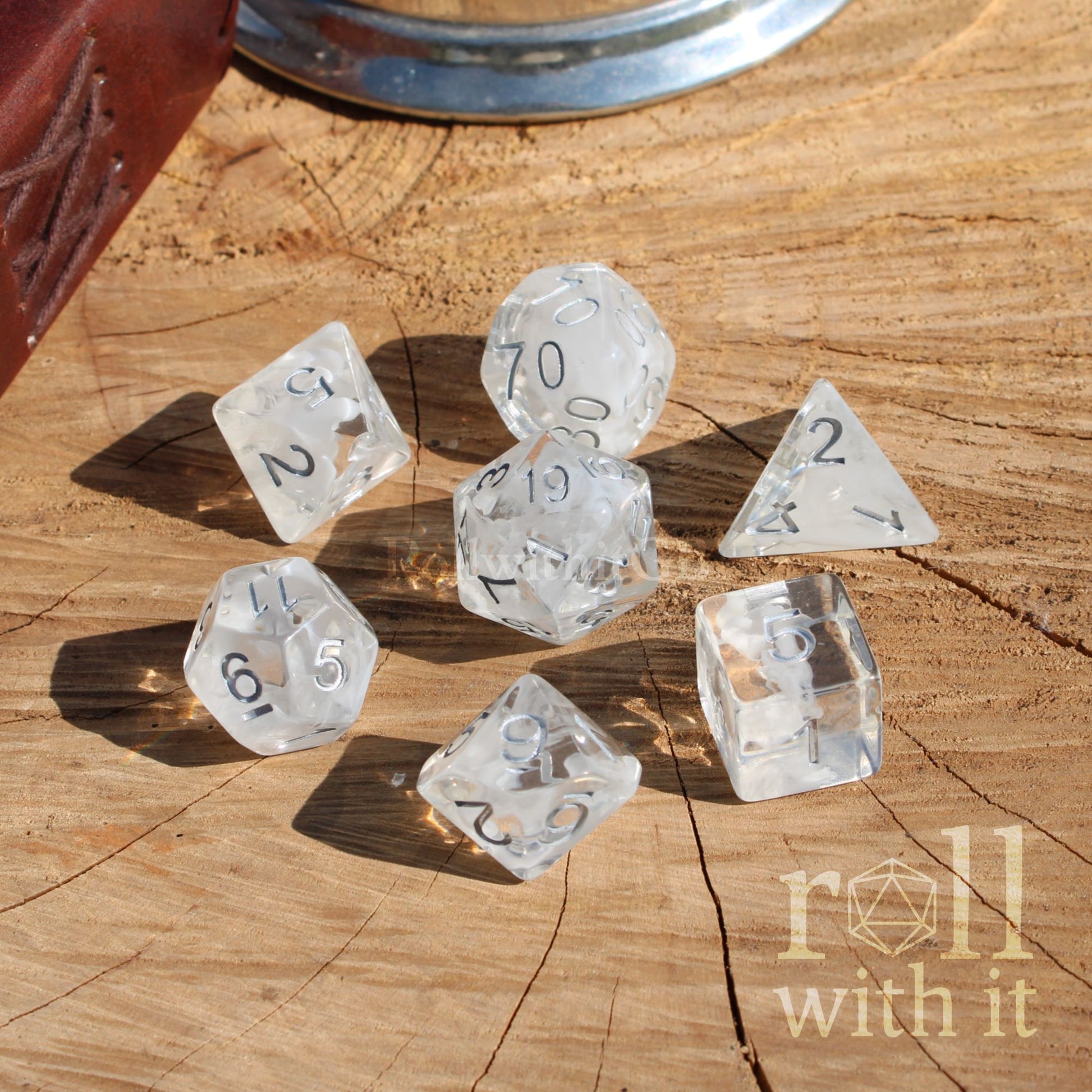 Clear white wisp plumes dice set on a wooden surface with 'roll with it' branding.