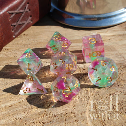 Set of colorful polyhedral dice with gold numbers on a wooden surface, featuring the brand 'roll with it'.