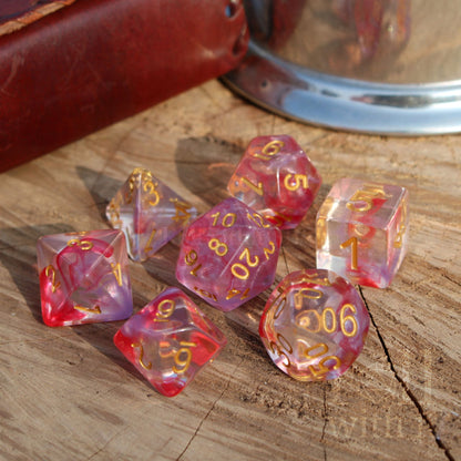 Set of 7 rose pink and clear polyhedral D&D dice with gold numbers on a wooden surface.