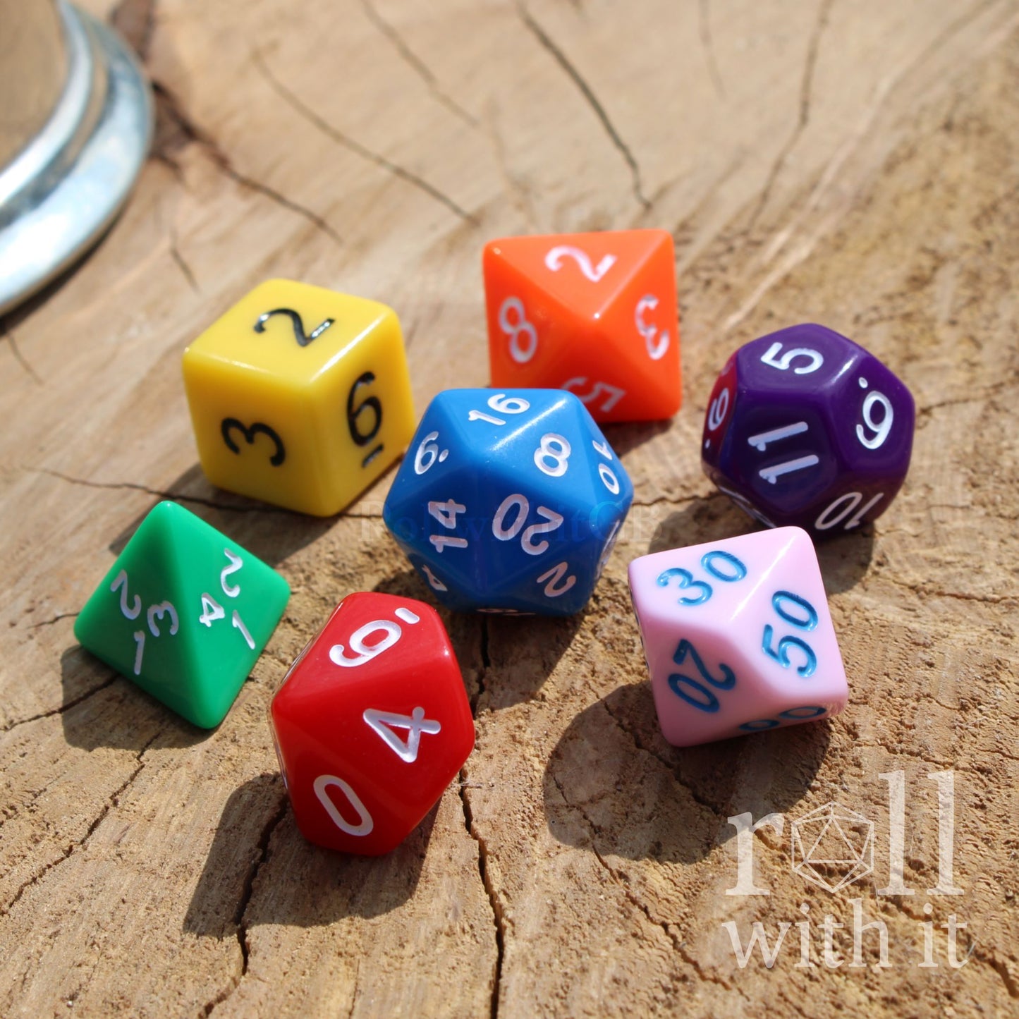 Colorful rainbow mixed polyhedral dice on a wooden surface with 'roll with it' text.
