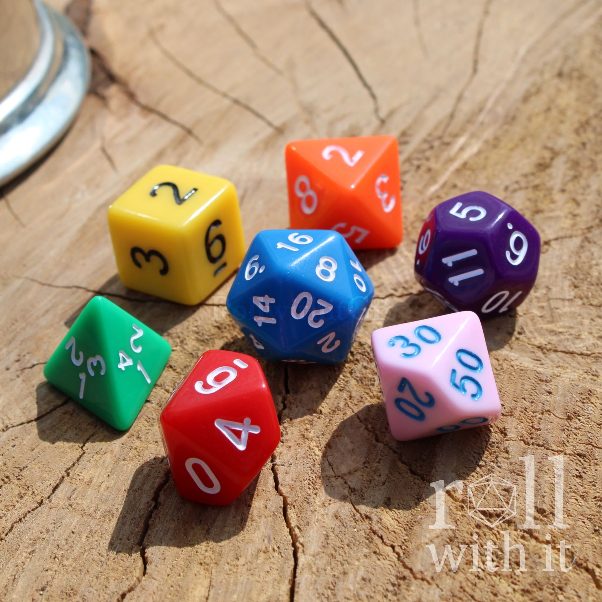 Colorful rainbow mixed polyhedral dice on a wooden surface with 'roll with it' text.