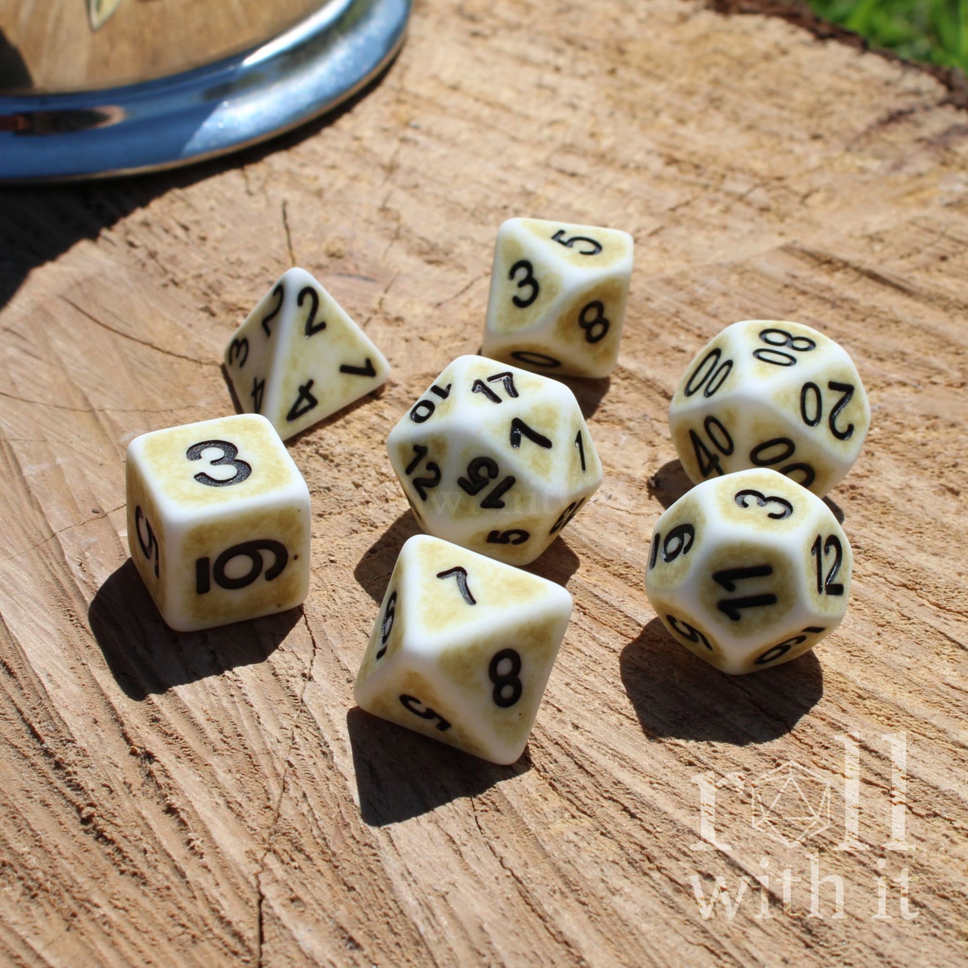 Angled view of 7 polyhedral white bone roleplaying TTRPG dice on a wooden surface with black easy to read letters