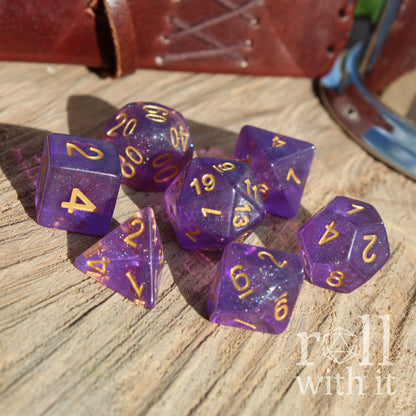Purple polyhedral dice set with gold numbers on a wooden surface, with 'roll with it' text.