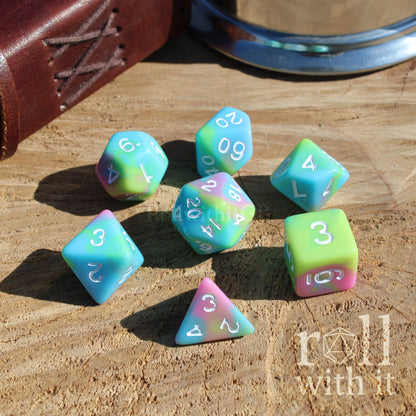 Angle view of 7 pastel rainbow tabletop roleplaying polyhedral dice set on a wooden surface with white ink