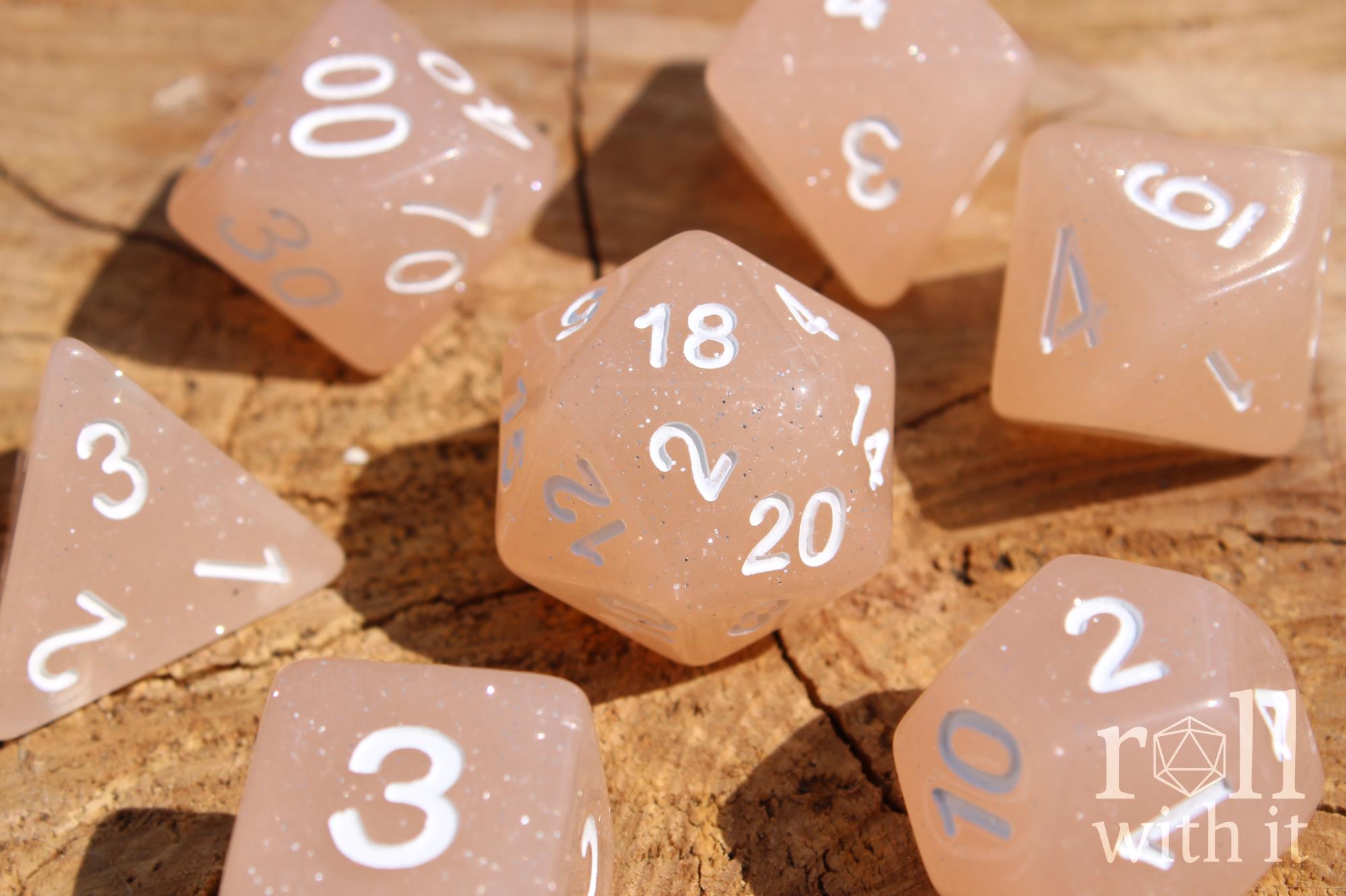Set of creamy beige glittery polyhedral dice with white numbers on a wooden surface