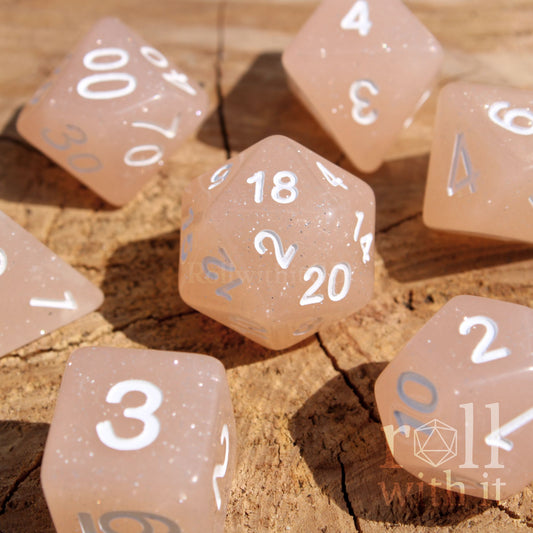 Set of creamy beige glittery polyhedral dice with white numbers on a wooden surface