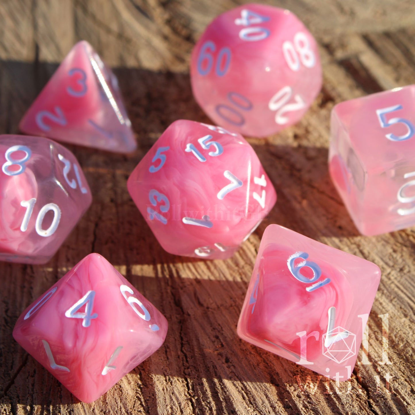Close up of 7 cute pastel pink fantasy cloudy aesthetic polyhedral tabletop roleplaying DND dice on a wooden surface