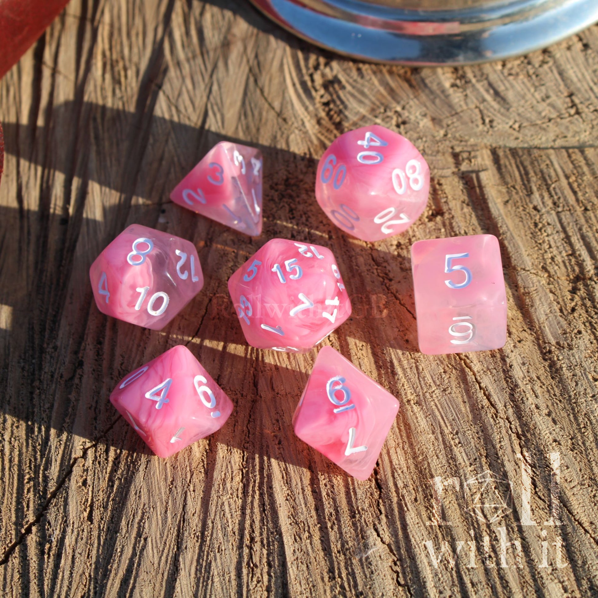 A set of 7 cute pastel pink polyhedral dice for tabletop roleplaying games on a wooden surface