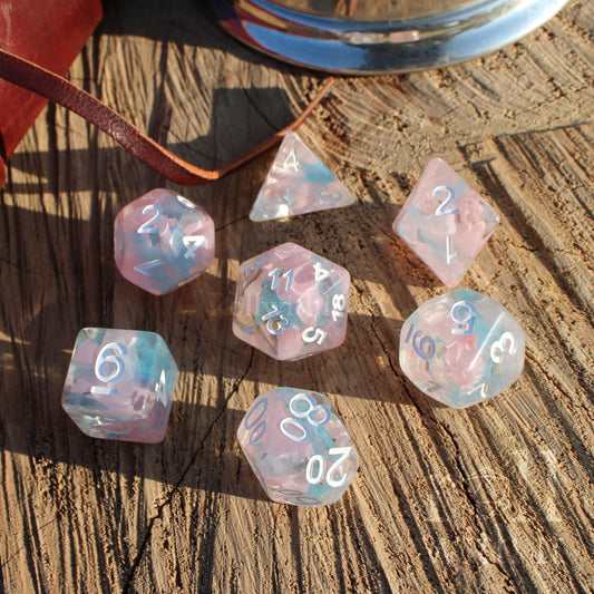 Set of 7 cute pale pink and blue ribbon swirling fantasy aesthetic D&D roleplaying game dice set on a wooden surface with white numbers