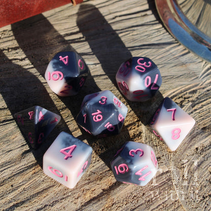 Set of 7 polyhedral tabletop RPG cute pink black pastel goth dice with pink numbers on a wooden surface