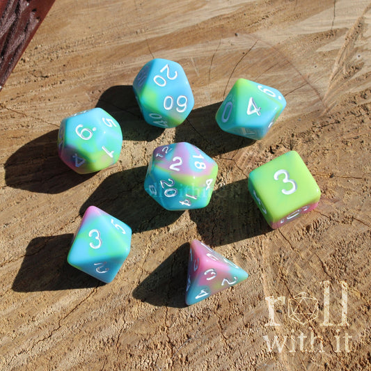 Top view of 7 cute pastel rainbow D&D polyhedral dice on a wooden surface with white numbers