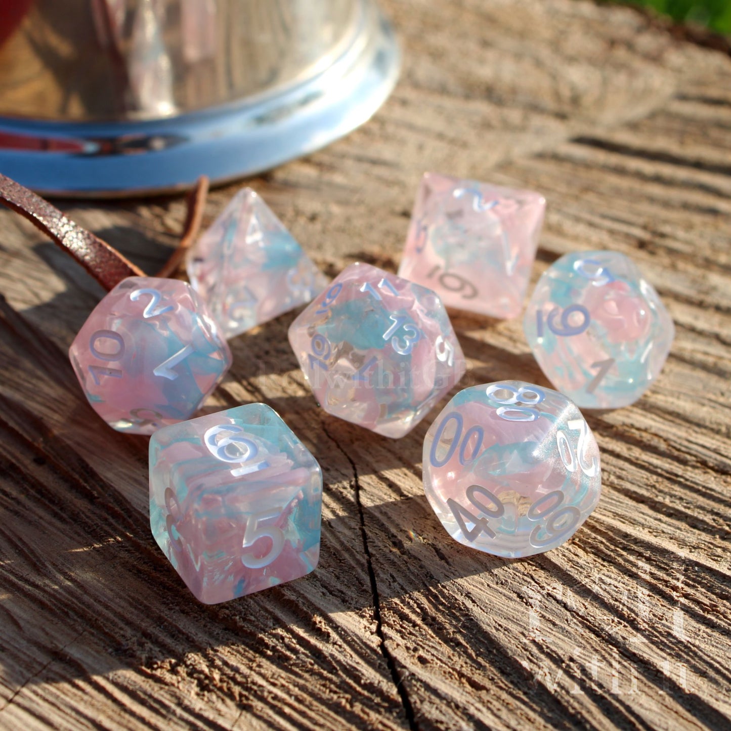 view of 7 Pathfinder pink blue clear swirling mixed colourful dice set with white numbers on a wooden surface