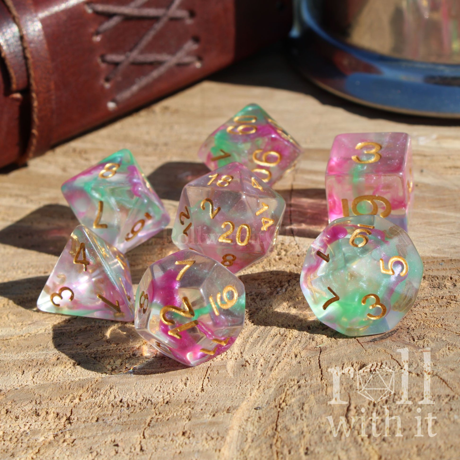 Set of colorful purple green glitter clear polyhedral dice with gold numbers on a wooden surface, featuring the text 'Roll with it'.