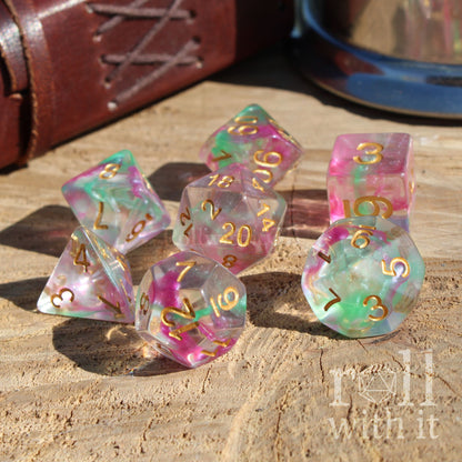 Set of colorful purple green glitter clear polyhedral dice with gold numbers on a wooden surface, featuring the text 'Roll with it'.