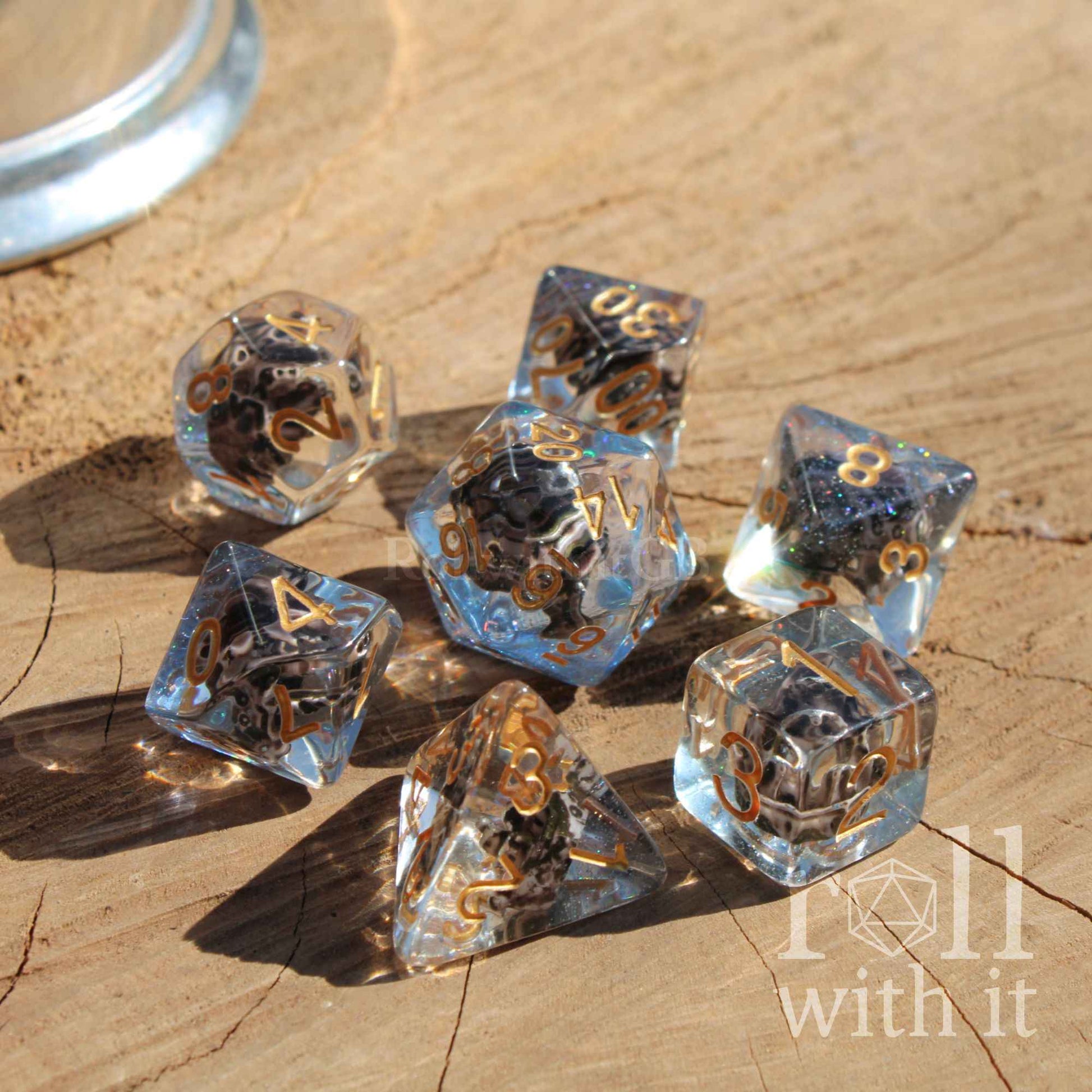 Complete set of 7 D&D dice on a wooden surface with glitter, blue, and pirate ship aesthetic on a surface
