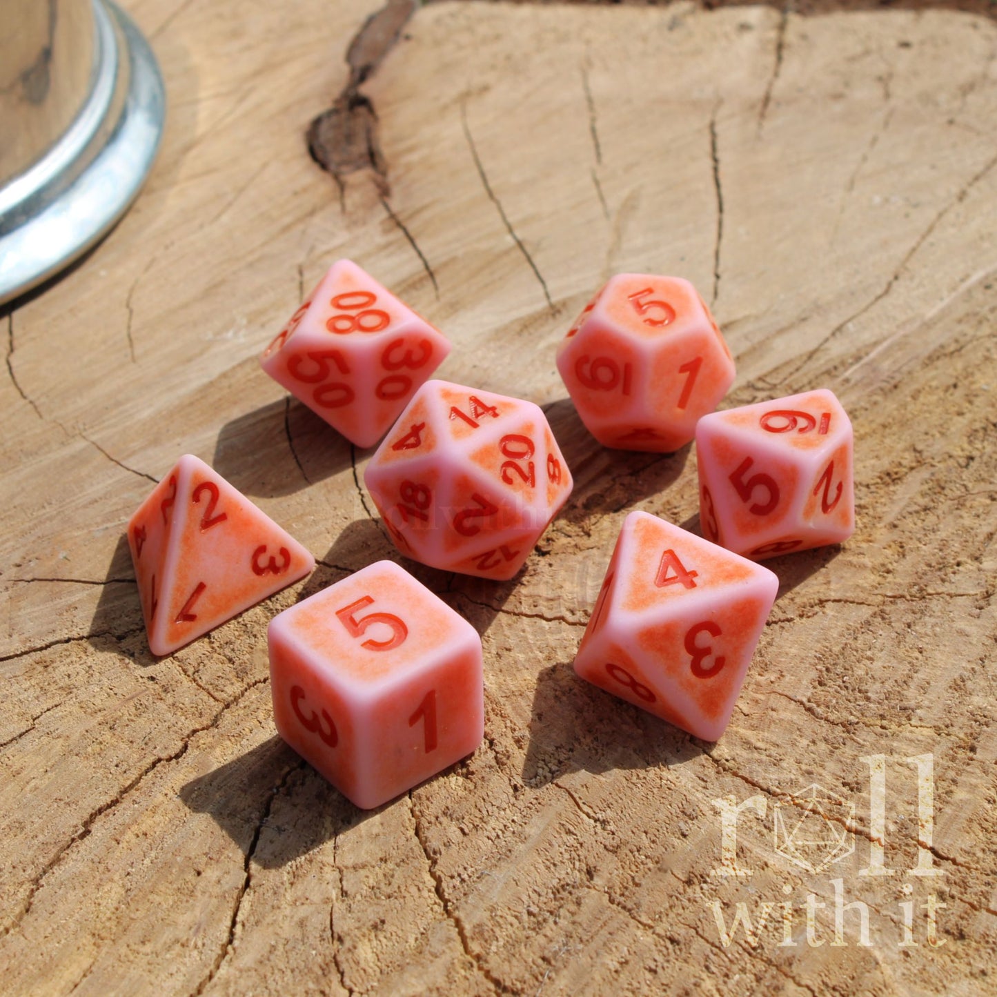 Set of pink polyhedral rolling playing dice on a wooden surface with 'roll with it' branding.