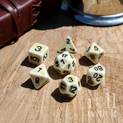 Set of 7 off white polyhedral playing dice on a wooden surface with 'roll with it' text.