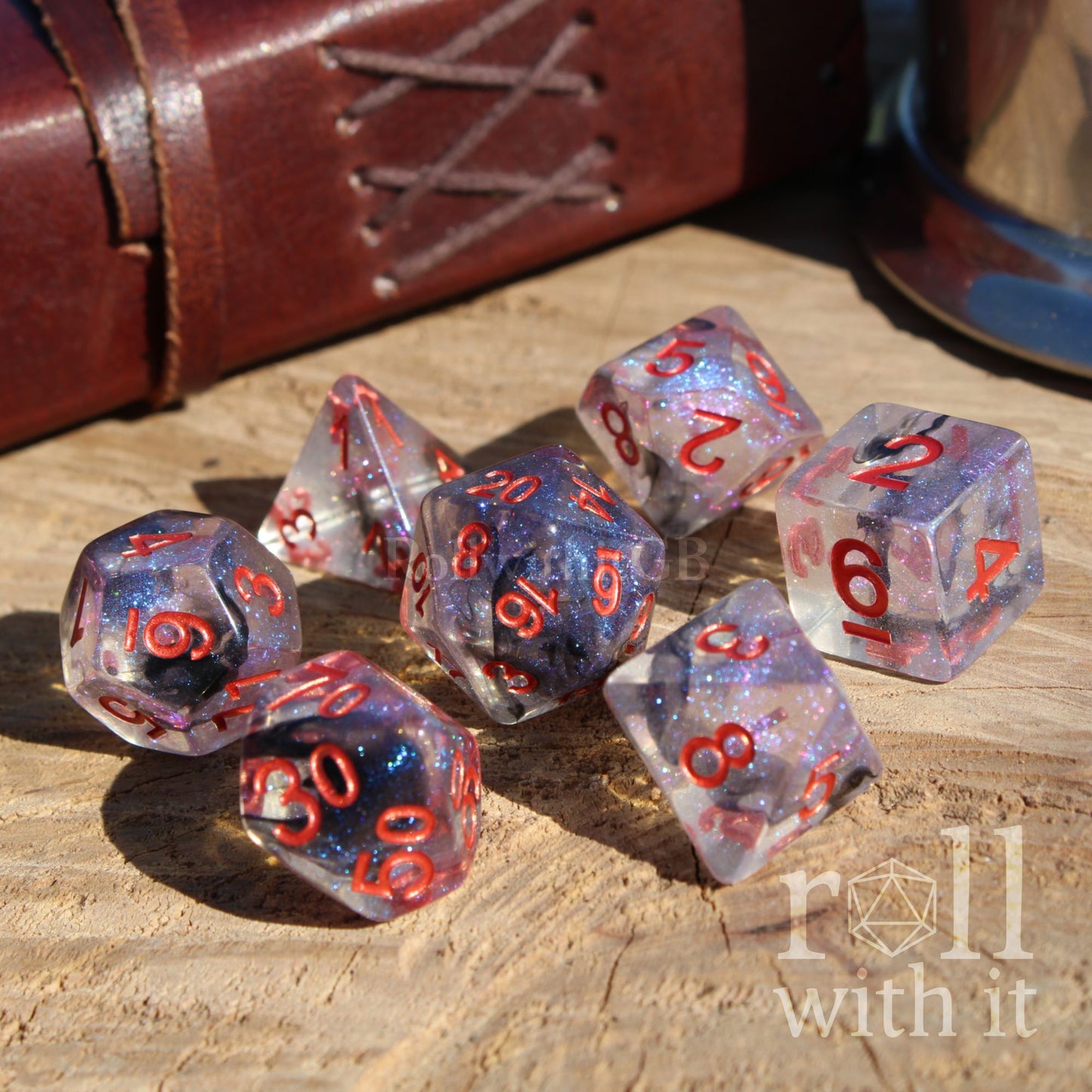 Set of 7 dark space galaxy purple polyhedral dice with red numbers on a wooden surface, with 'roll with it' branding.