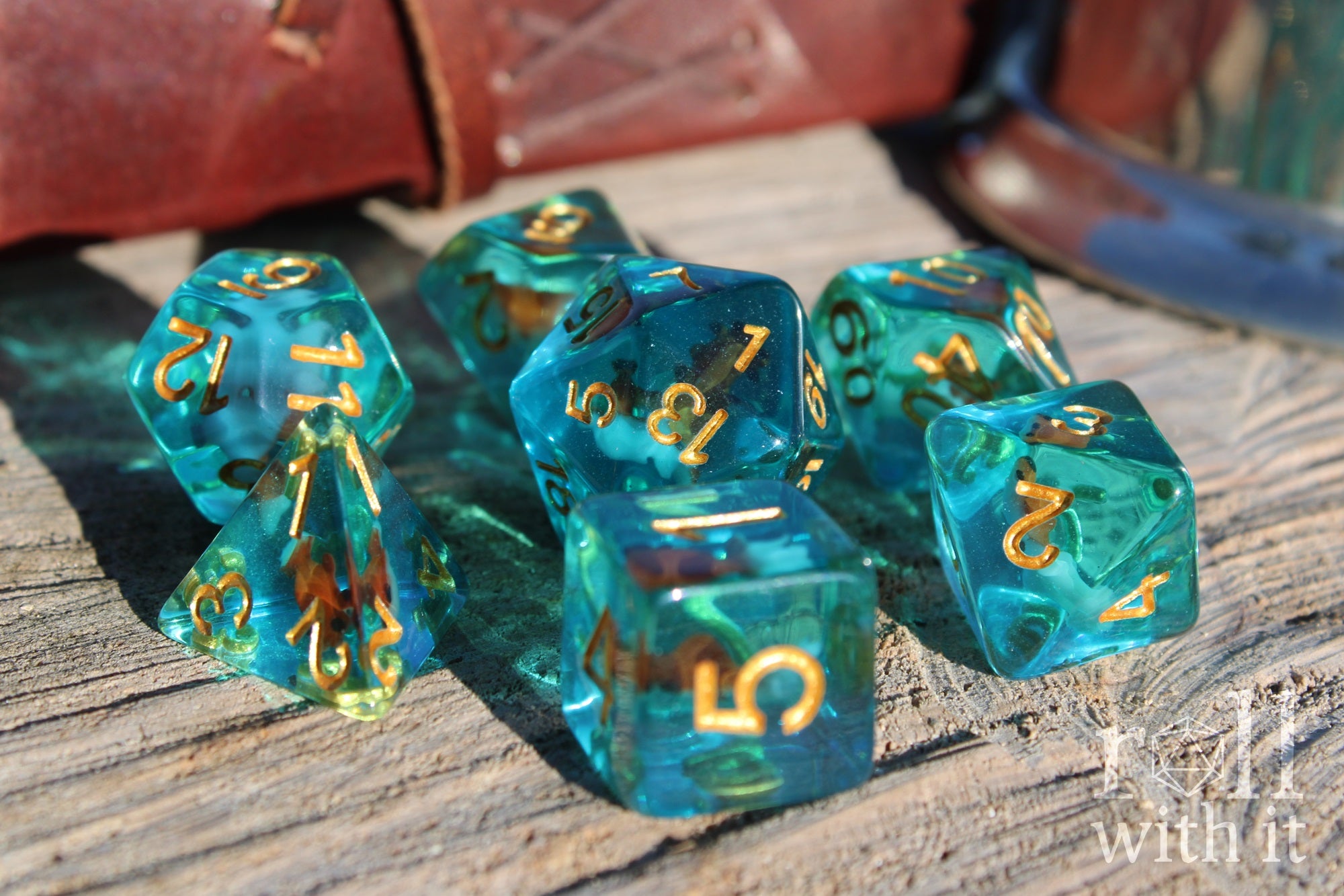 Set of clear blue turquoise polyhedral dice with gold numbers and a mini goldfish inside on a wooden surface