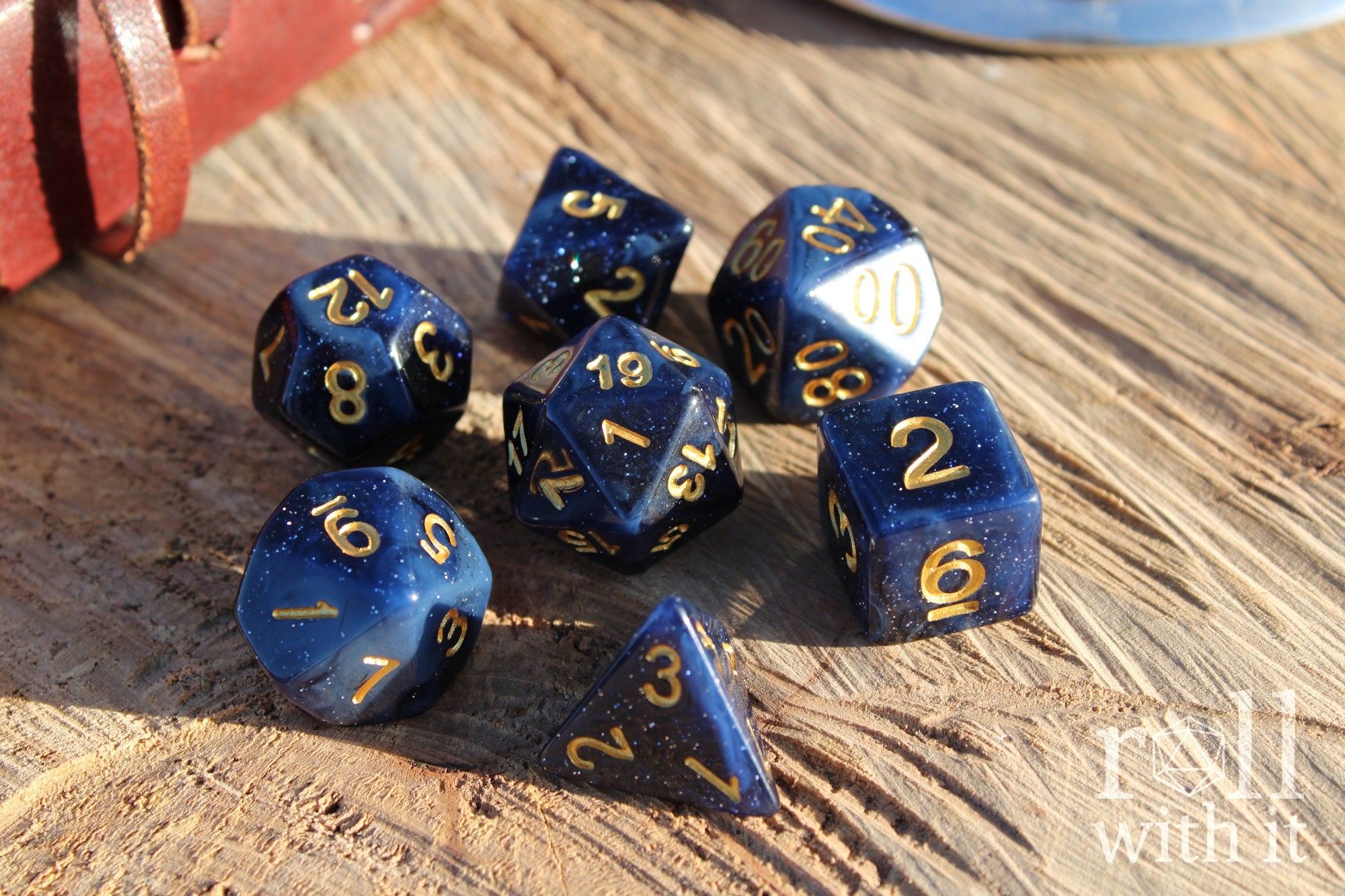 Deep midnight blue polyhedral starry glittery roleplaying dice with gold numbers on a wooden surface