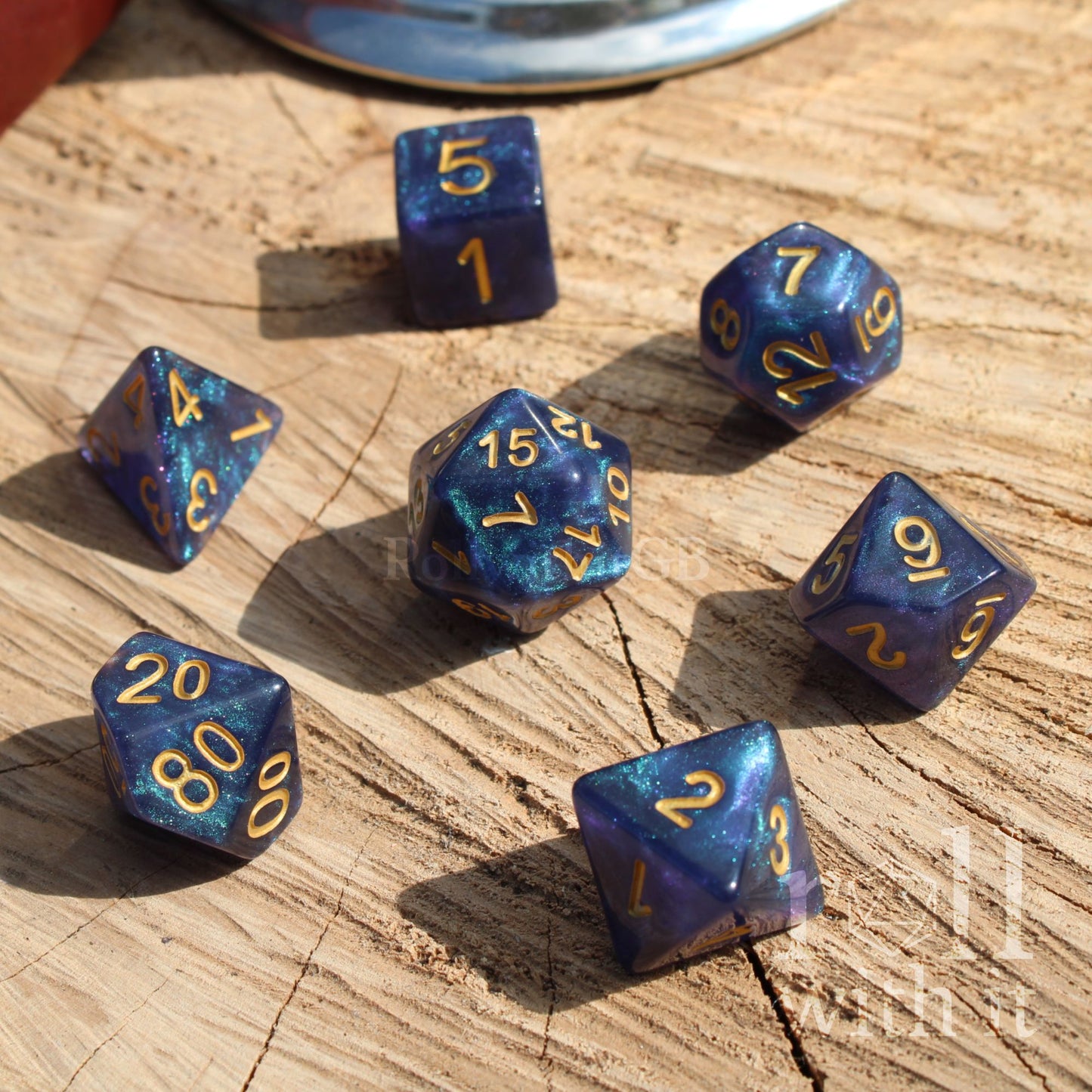 Full set of 7 dark glitter filled and shiny blue polyhedral TTRPG dice set with gold numbers on a wooden surface