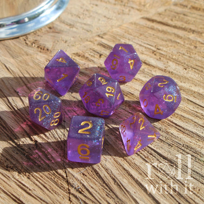Purple polyhedral dice set with gold numbers on a wooden surface, featuring the 'roll with it' logo.