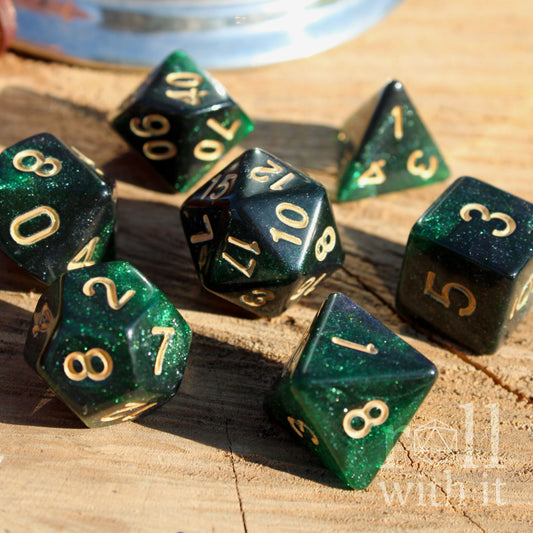 Set of 7 galaxy starry emerald green glittery polyhedral dice with gold numbers on a wooden surface