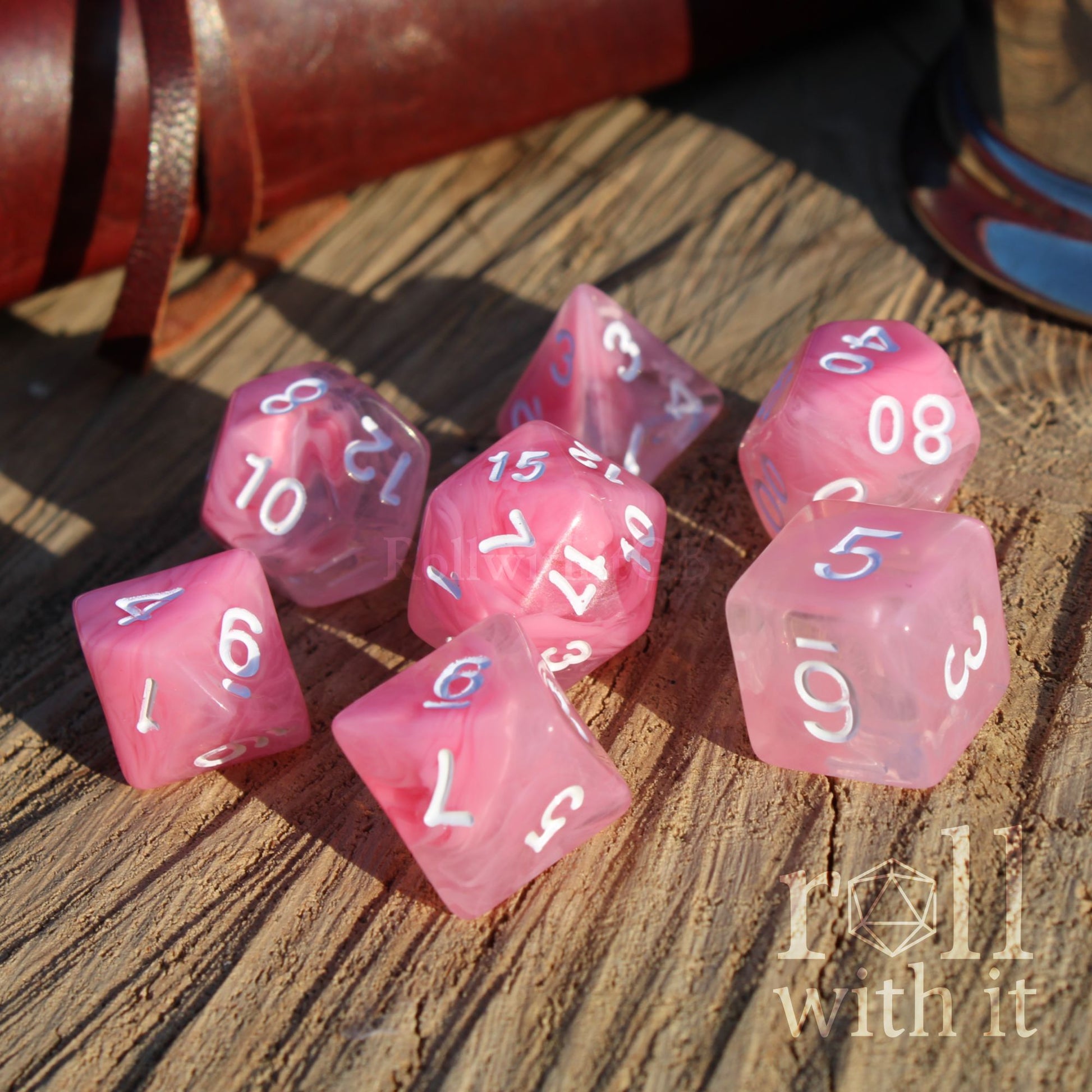 Cute cloudy pink polyhedral D&d dice set on a wooden surface with 'roll with it' text.