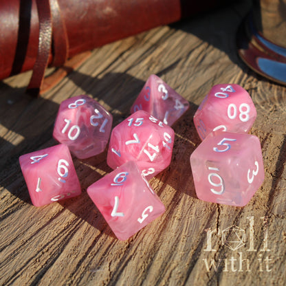 Cute cloudy pink polyhedral D&d dice set on a wooden surface with 'roll with it' text.